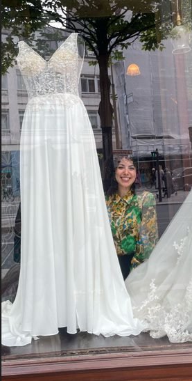 Mouna dans la vitrine de MADAMOON, à côté d'une robe de mariée en dentelle